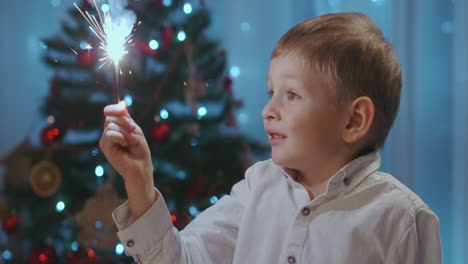 A-boy-holds-and-looks-joyfully-at-a-sparkler-sitting-at-dinner-on-Christmas-Eve.-Celebrate-the-new-year-with-sparklers.-Boy-3-5-holds-a-Sparkler-fire.-High-quality-4k-footage